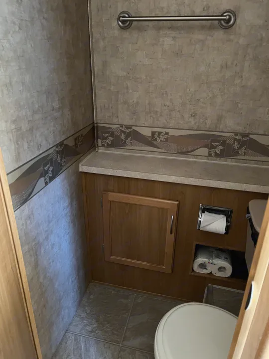 This RV rental bathroom features a toilet, storage cabinet, counter, towel bar, and decorative wallpaper with a border.. Ford Bounder 2008