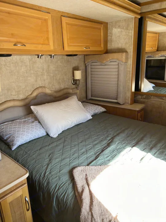 RV rental bedroom featuring a bed with quilted comforter, overhead cabinets, and window. Ideal for road trips.. Ford Bounder 2008