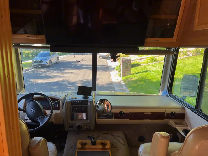 Inside an RV rental: driver's view from the cockpit, dashboard, steering wheel, looking out onto a residential street with parked cars.. Ford Bounder 2008
