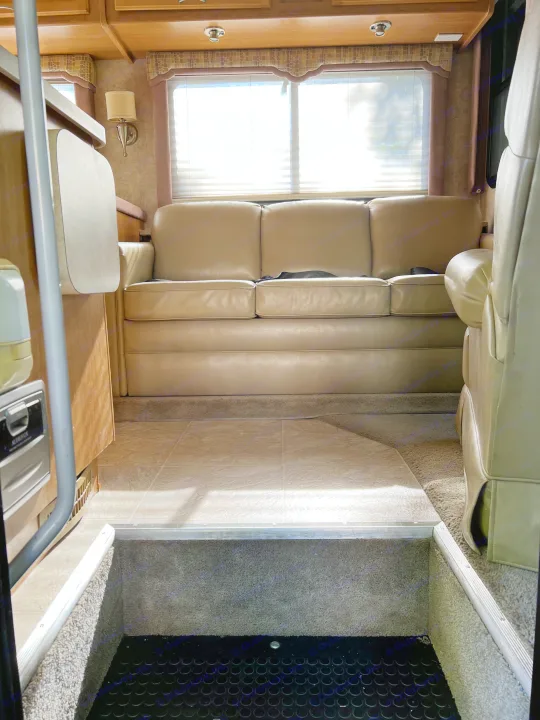 This RV rental offers a comfortable living space with a tan sofa, blinds on the windows, and multi-level flooring.. Ford Bounder 2008