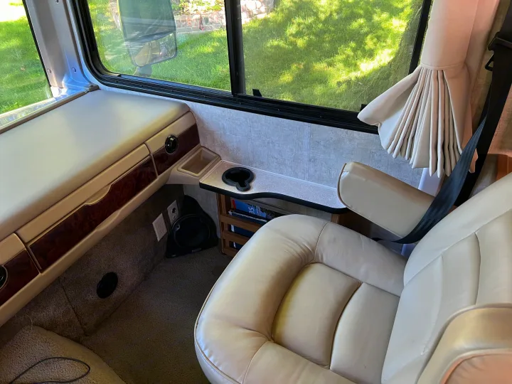 Inside a spacious rv rental: light-colored leather passenger seat, wide window with green outdoor view, and convenient built-in cupholders.. Ford Bounder 2008