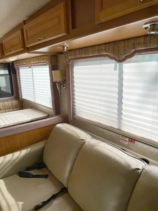 Inside an RV rental: a sunlit living area with pleated window blinds, comfortable sofa, overhead cabinets, and dining nook.. Ford Bounder 2008