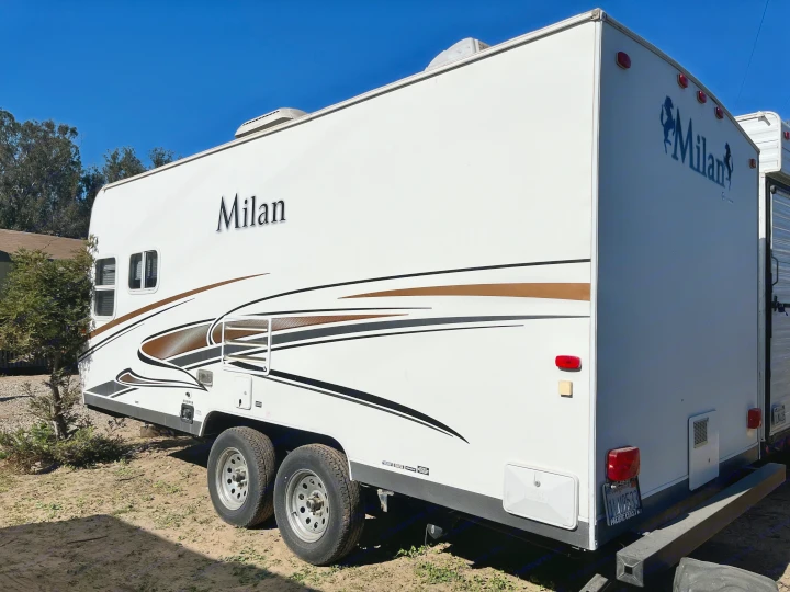White Milan travel trailer RV rental, featuring brown and black graphic stripes, parked under a clear blue sky.. Eclipse Recreational Vehicles Milan 2011