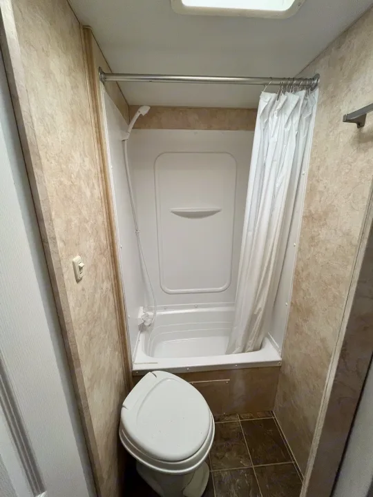 Compact RV bathroom: toilet, shower/tub, and curtain, ideal for an RV rental. Efficient, space-saving design.. Eclipse Recreational Vehicles Milan 2011