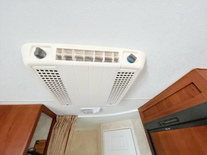 Inside an **rv rental**, a ceiling-mounted AC unit with fan speed and temp controls. Brown cabinetry, door, and curtain visible.. Eclipse Recreational Vehicles Milan 2011
