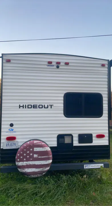 This RV rental, a Keystone Hideout travel trailer, shows its back with an American flag tire cover and KY plate.. Keystone RV Hideout 2022