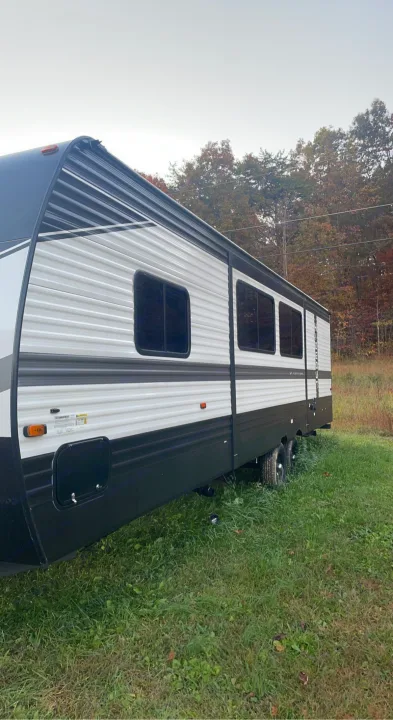 White & black RV rental parked on grass. Ideal for travel, outdoor adventures against autumn trees.. Keystone RV Hideout 2022