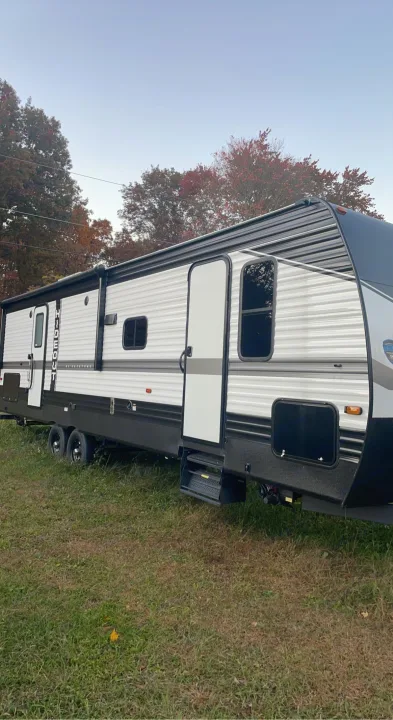 Modern white and gray Hideout travel trailer RV rental with awning extended, parked on grass on an autumn day.. Keystone RV Hideout 2022