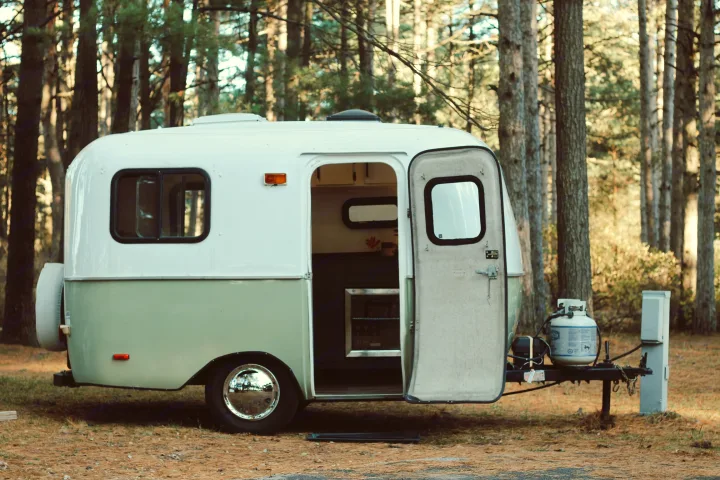 Charming white & green rv rental awaits in a peaceful forest. Its open door reveals an inviting space for camping adventures.. Scamp Scamp Trailer 2005