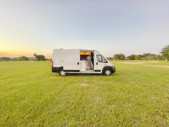 Freedom awaits with an RV rental! A person in their camper van, parked in a grassy field at sunset.. Other Other 2020