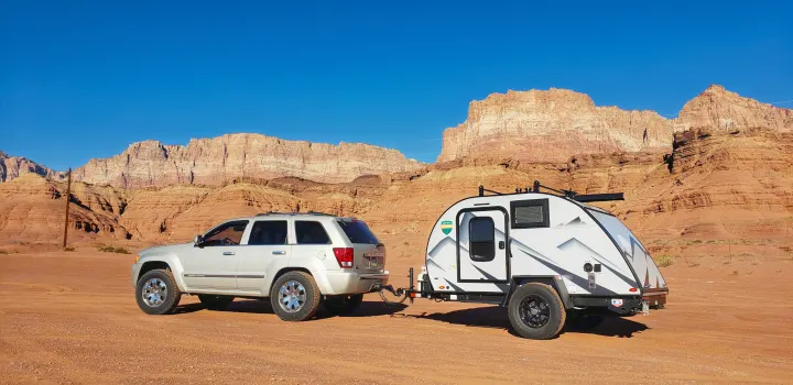 SUV towing a teardrop RV rental in a stunning desert landscape with red rock mountains. Perfect for an outdoor adventure!. Braxton Creek Free Solo 2022