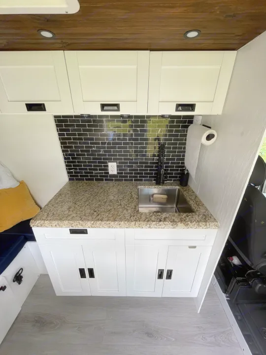 Modern RV rental kitchen: white cabinets, granite countertop, black subway tile backsplash, stainless sink, and wooden ceiling.. Other Other 2020