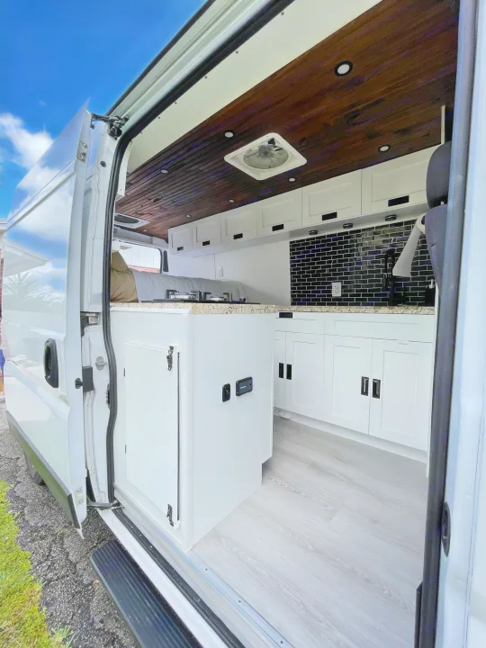 Spacious RV rental interior showcasing a dark wood ceiling, white kitchen with black backsplash, and light wood-look flooring.. Other Other 2020