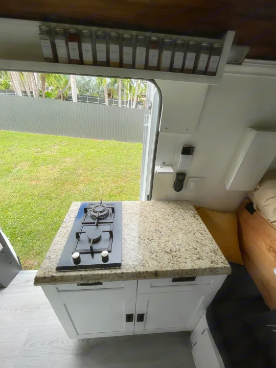 RV rental: A compact van kitchen featuring a built-in stove, granite countertop, spice rack, and an open door view to a green yard.. Other Other 2020