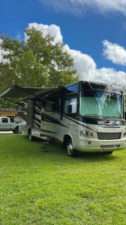 A large motorhome RV rental, light-colored with dark accents, parked on a sunny green lawn with. Forest Rivers Georgetown 2013