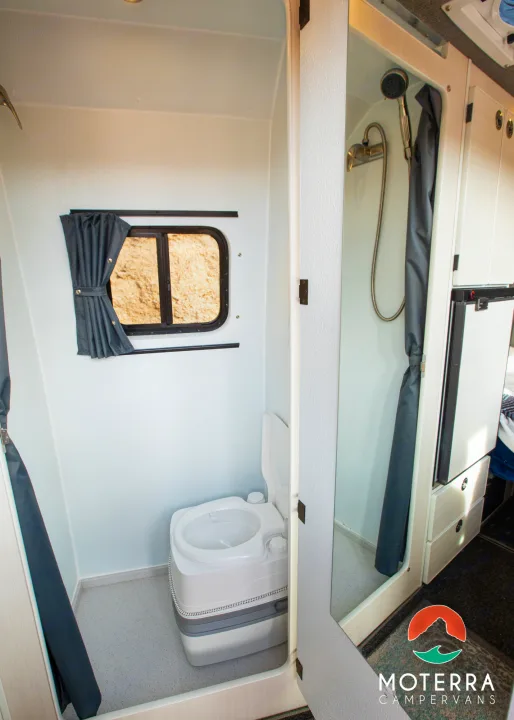 Compact RV rental wet bath featuring a portable toilet, window with curtain, and a separate shower area. Practical campervan interior.. Mercedes-Benz Sprinter 2021