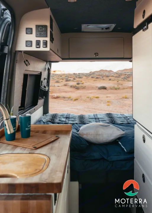 This RV rental interior offers a kitchen area, comfortable bed, and expansive desert views from open back doors.. Mercedes-Benz Sprinter 2021