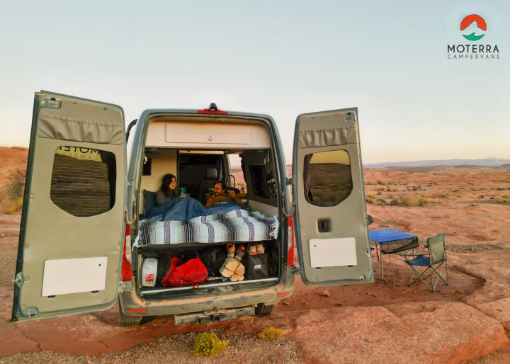 Two people relaxing in a Moterra RV rental campervan with open doors, overlooking a vast desert landscape. Ideal for camping.. Mercedes-Benz Sprinter 2021
