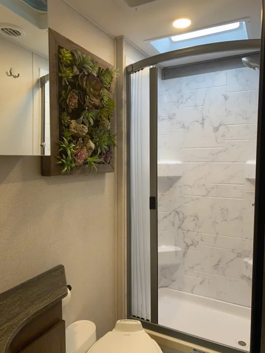 Modern RV rental bathroom: enjoy a spacious shower, bright lighting, mirror, toilet, and charming succulent wall art.. Forest River Sunseeker 2022