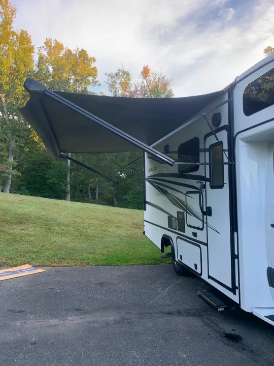 RV rental with its black awning fully extended, parked on asphalt with trees in the background. Ready for relaxation.. Forest River Sunseeker 2022