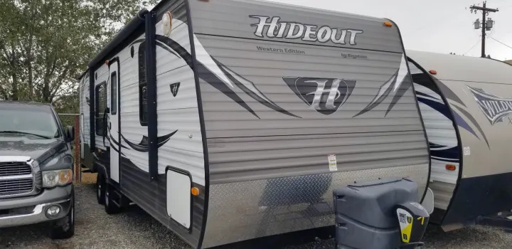 Gray Hideout travel trailer (RV rental) parked in a lot, with a truck nearby and another RV visible.. Keystone RV Hideout 2015