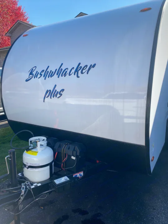 Front view of a white Bushwhacker Plus travel trailer with a propane tank and batteries, ideal for your next rv rental trip.. Braxton Creek Bushwhacker Plus 2022