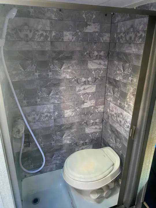 This RV rental features a small wet bath with gray marble-style wall tiles, a shower hose, and a compact toilet.. Braxton Creek Bushwhacker Plus 2022