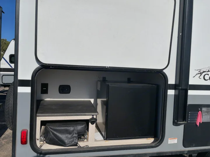 RV rental's outdoor kitchen area: open hatch, mini-fridge, counter, power outlets, bottle opener, and storage.. Coachmen Apex 208BHS 2023