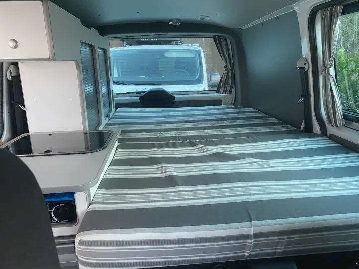 Cozy campervan interior: striped bed, kitchen & storage. Perfect for an RV rental adventure.. Volkswagen Transporter T6.1 2021