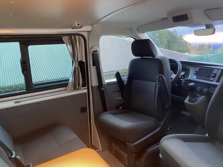 RV rental's comfortable camper van interior, featuring seating, table, window with curtains, and a scenic front view.. Volkswagen Transporter T6.1 2021