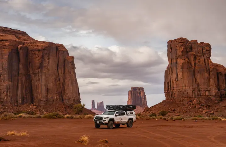 A white Toyota Tacoma overlanding truck, ideal for an RV rental adventure, parked among iconic red rock formations in Monument Valley.. Toyota Tacoma 2022