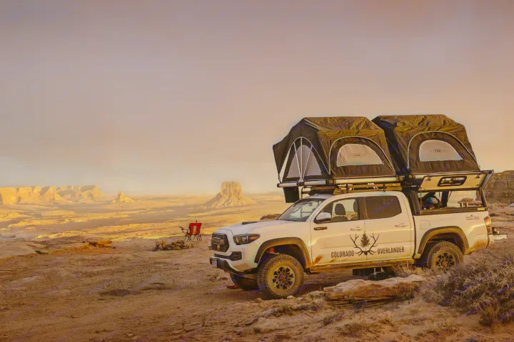 White overlanding truck with roof-top tents deployed for camping in a vast desert at sunset. A rugged outdoor RV rental experience.. Toyota Tacoma 2022