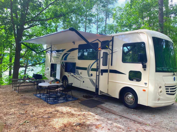 Relax at this beautiful rv rental campsite! A Holiday Rambler motorhome by the lake, with outdoor dining under a shaded awning.. Holiday Rambler Admiral 2021