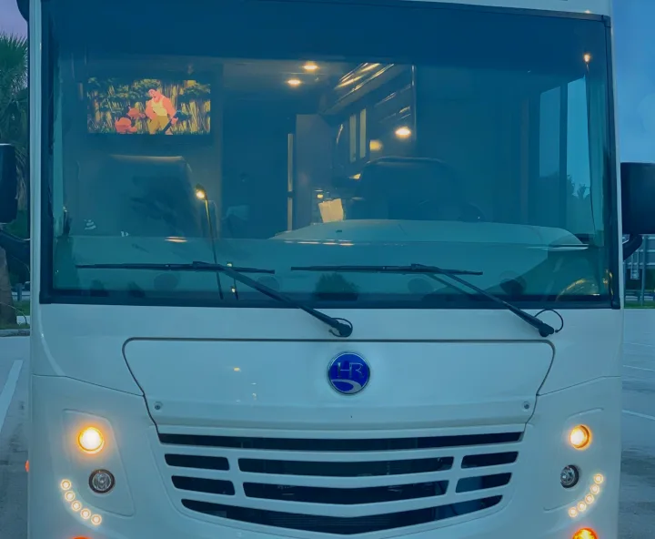 Bright white RV rental, front view. Inside, an animated movie plays on a TV visible through the windshield.. Holiday Rambler Admiral 2021