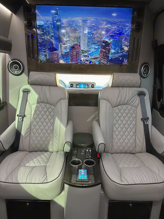 Luxurious RV rental interior: large screen TV, plush quilted captain's chairs, & integrated tech for premium comfort.. Midwest Automotive Designs Ultimate Coach 2023