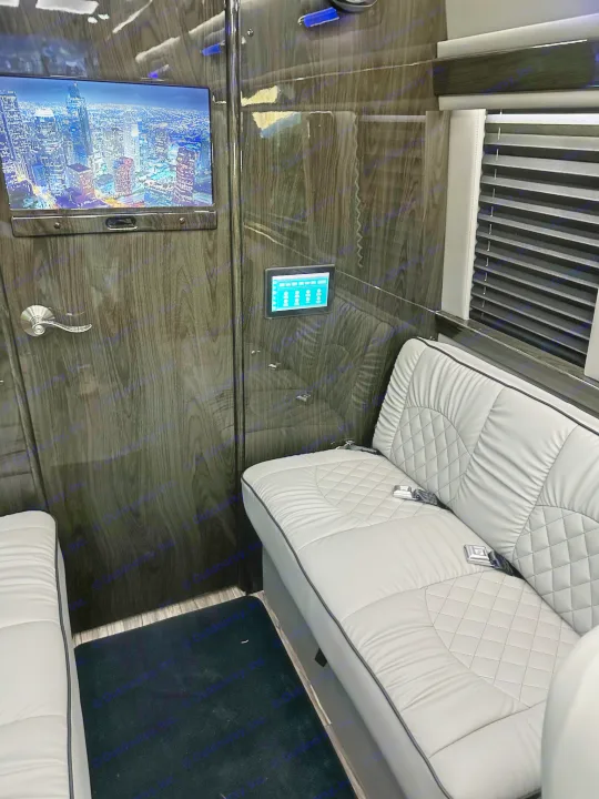 Luxurious RV rental interior: featuring a large TV, touch control panel, and plush grey quilted leather seating.. Midwest Automotive Designs Ultimate Coach 2023