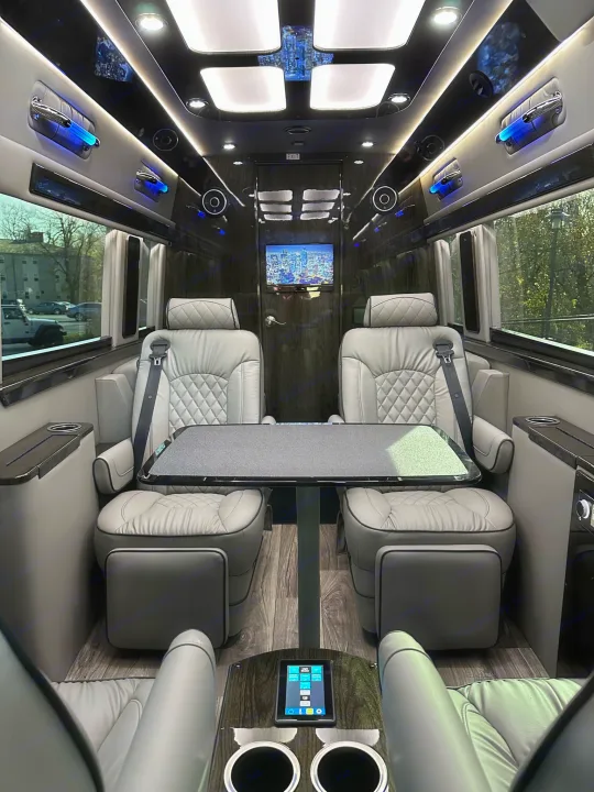 Luxurious RV rental interior, showcasing plush, quilted seating, a central table, and a TV screen for comfortable travel.. Midwest Automotive Designs Ultimate Coach 2023
