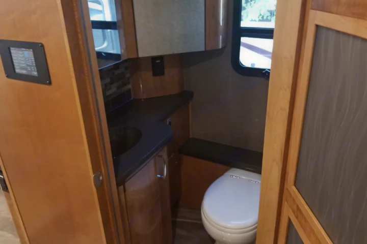 Interior view of an RV rental bathroom, showcasing a toilet, sink vanity, and control panel on light wood cabinetry.. American Coach American Eagle 2017