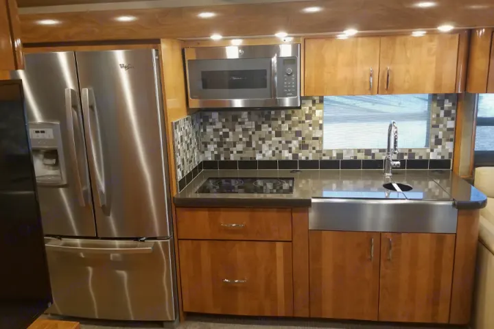 Modern kitchen in an RV rental featuring stainless steel refrigerator, microwave, cooktop, and farmhouse sink.. American Coach American Eagle 2017