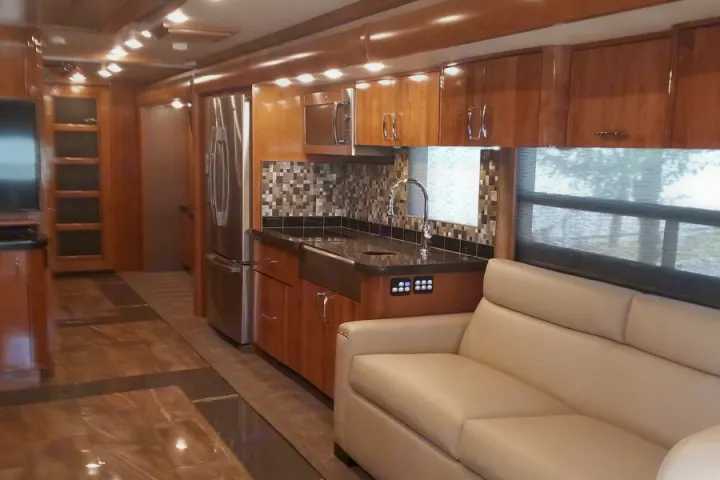 Spacious luxury RV rental interior with modern kitchen, stainless steel appliances, wood cabinetry, and comfy sofa.. American Coach American Eagle 2017