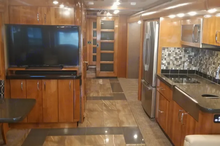 Modern RV rental interior featuring a full kitchen, entertainment center with TV, and sleek wood cabinetry.. American Coach American Eagle 2017