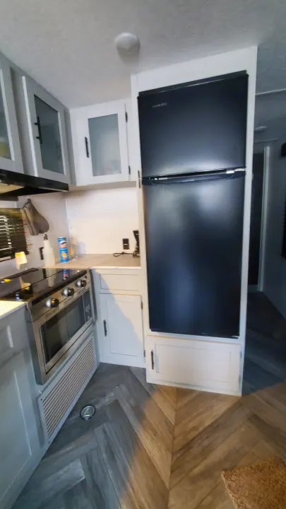 This RV rental features a compact kitchen with a modern black refrigerator, microwave, and stove for convenient cooking.. Forest River Wildwood 2022