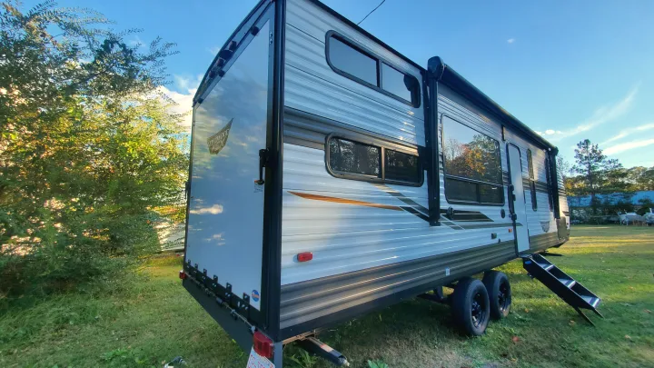This travel trailer looks ready for an RV rental adventure, parked on green grass under a blue sky.. Forest River Wildwood 2022