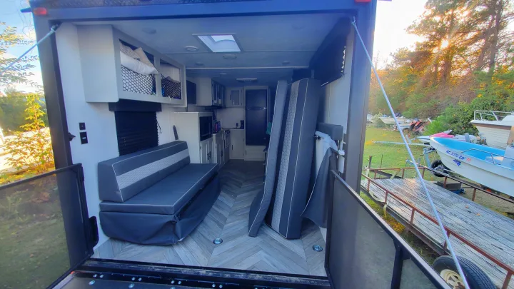 Spacious RV rental toy hauler with open ramp, revealing kitchen, seating, and bunks, looking out to boats.. Forest River Wildwood 2022