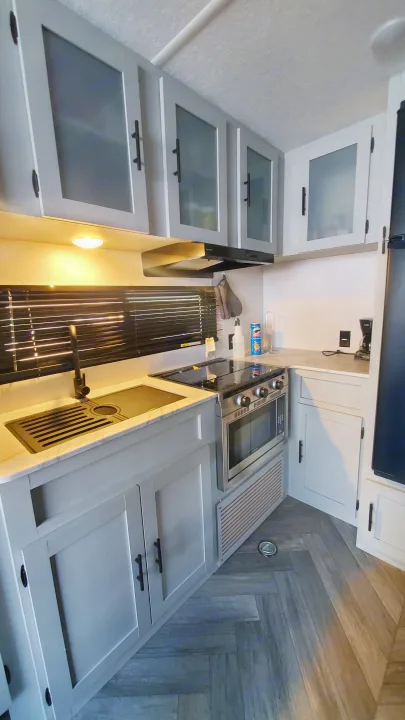 Modern RV rental kitchen with light gray cabinets, sink, stove, oven, and microwave. A compact, functional space.. Forest River Wildwood 2022
