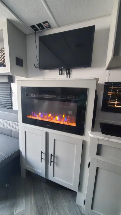 Modern RV rental interior featuring a flat-screen TV above an electric fireplace with a cozy dinette and light cabinetry.. Forest River Wildwood 2022