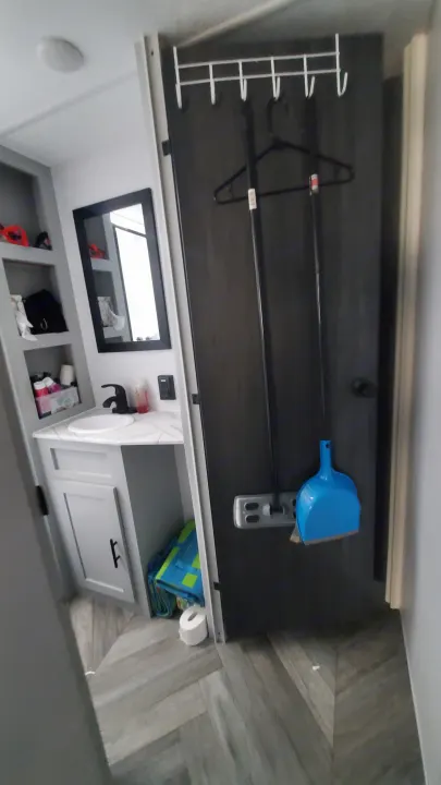 View of a functional RV rental space, showing a small bathroom with vanity and a door equipped with cleaning tools.. Forest River Wildwood 2022