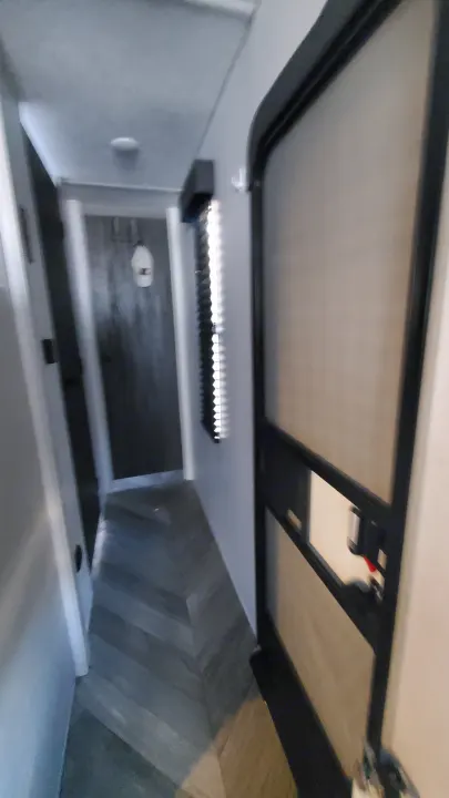 Inside an RV rental, a narrow hallway features herringbone flooring, a screen door on the right, and a dark door ahead.. Forest River Wildwood 2022