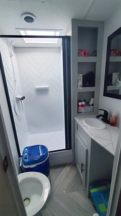 RV rental bathroom: white shower (herringbone walls), toilet, vanity, and a blue portable washing machine inside the shower.. Forest River Wildwood 2022