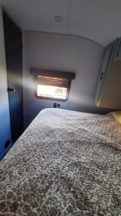 Cozy RV rental bedroom featuring a bed with patterned comforter, window, and overhead storage for your trip.. Forest River Wildwood 2022
